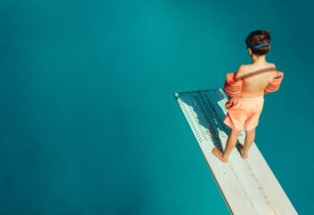 Top view of boy standing on spring board learning to dive during swimming class on a summer day. Boy learning swimming at outdoor pool.