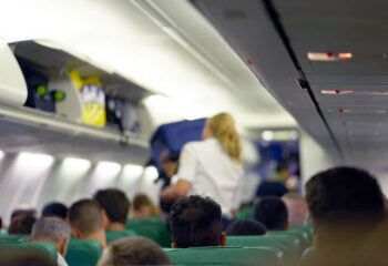 a flight attendant lifting luggage into the overhead compartment in the cabin of an airplane filled with passengers