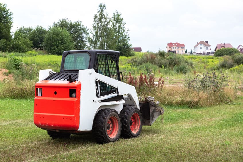 A skid steer loader clears the site for construction. Land work by the territory improvement. Machine for work in confined areas. Small tractor with a bucket for moving soil, turf and bulk materials.