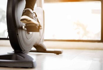 Close up foot biking in gym, exercising legs doing cardio workout cycling bikes.