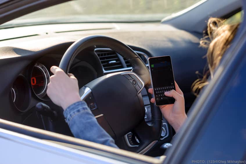 view through the open side window from behind a driver in a car as they read an sms or text message on a mobile phone, blank screen visible