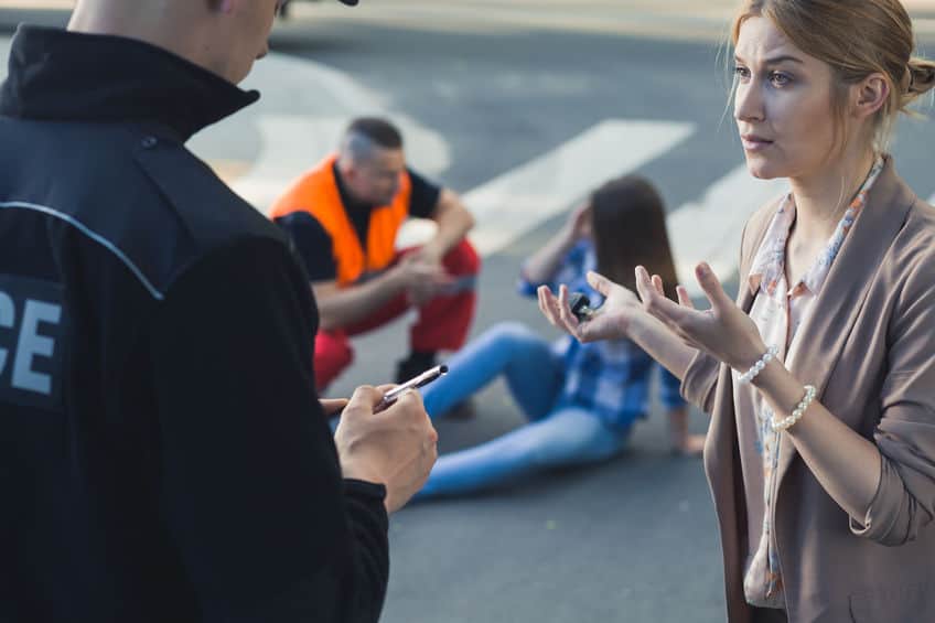witness to a car accident talking with the police officer with victim of the car accident in the background